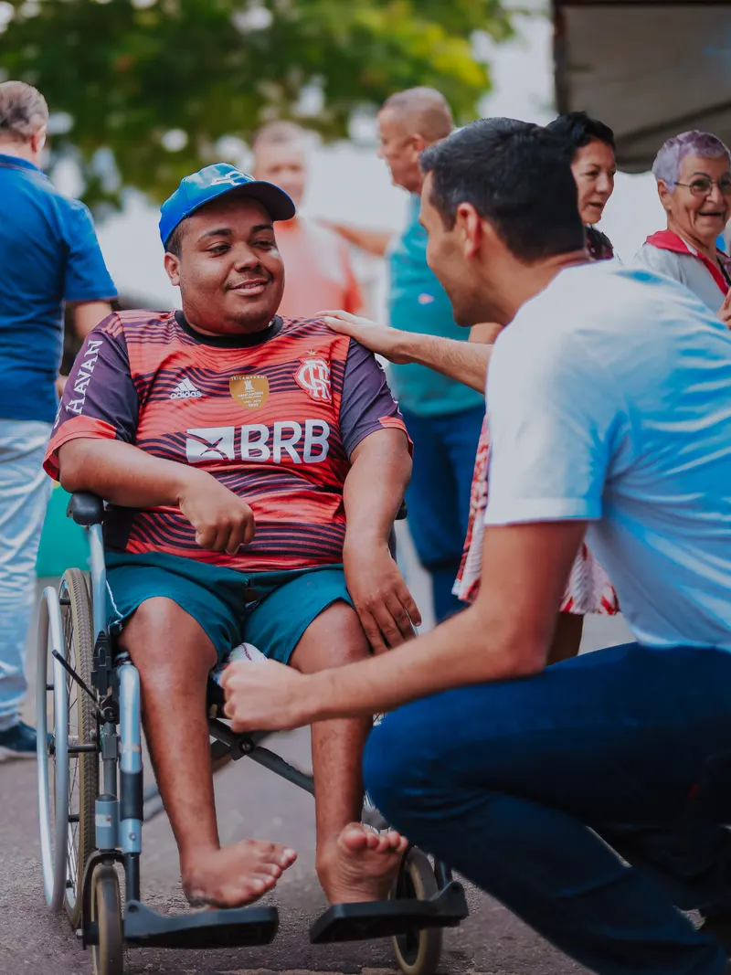 Serginho Vidigal agachado conversando com um jovem cadeirante em uma rua