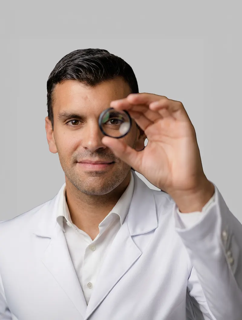 Serginho Vidigal sorrindo enquanto segura uma lente de oftalmologia diante do olho