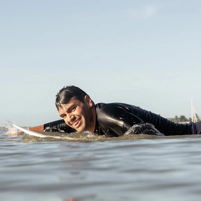 Serginho Vidigal sorrindo deitado na prancha de surfe no mar